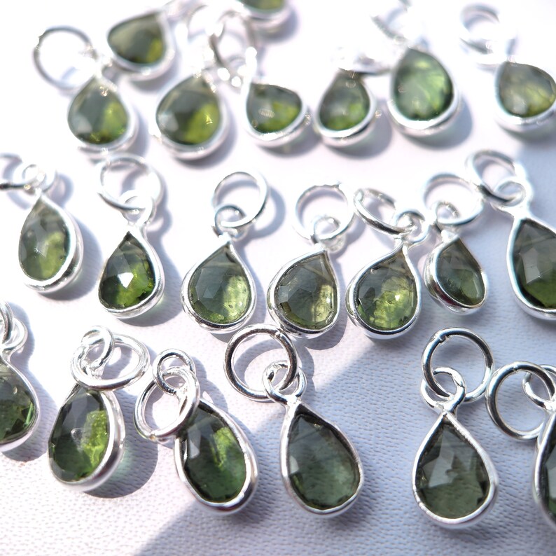 Op de afbeelding: Een verzameling zilveren hangers in druppelvorm met groene edelsteenaccenten. De hangers hebben een lus aan de bovenkant om aan sieraden te bevestigen.