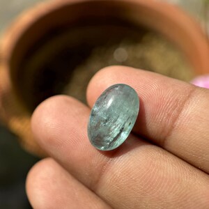 May include: A light blue oval-shaped aquamarine gemstone with a smooth, polished surface.