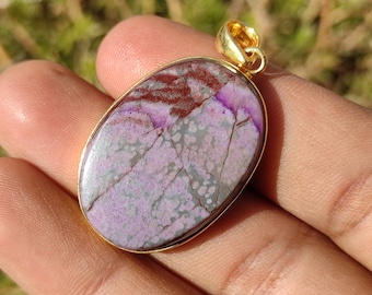 Pode incluir: Pingente oval com uma configuração de ouro e uma pedra roxa, marrom e branca.