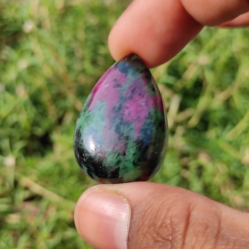 May include: A teardrop-shaped green, black, and pink gemstone pendant.