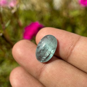 May include: A light blue oval-shaped aquamarine gemstone with a smooth, polished surface. The stone has a translucent appearance with visible internal inclusions.