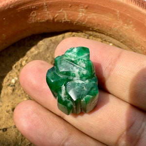 May include: A carved green gemstone with white veins, resembling a stylized leaf or flower.
