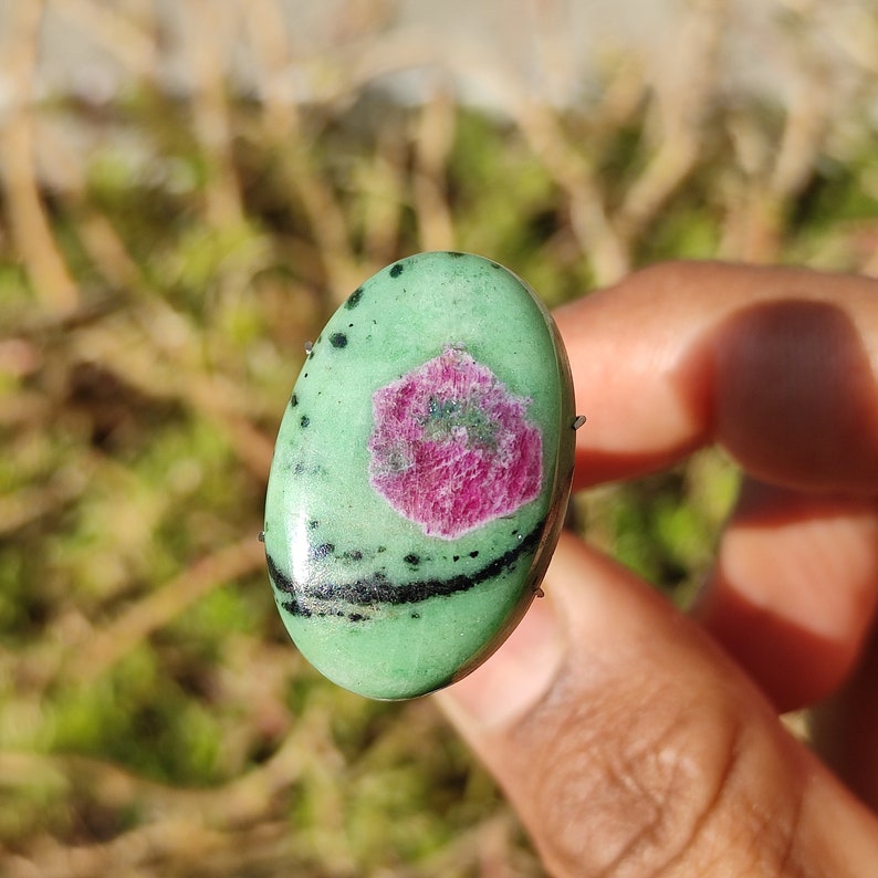 Peut inclure: Pierre pr&eacute;cieuse verte de forme ovale avec des inclusions noires et une inclusion en forme d'&eacute;toile rose et verte au centre.