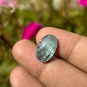 May include: A light blue oval-shaped gemstone with a smooth, polished surface. The gemstone has a translucent appearance with visible internal inclusions.