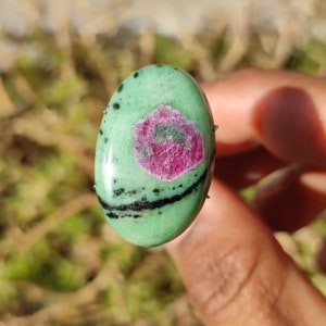 Peut inclure: Une pierre pr&eacute;cieuse ovale verte en cabochon avec des inclusions noires et une inclusion de rubis rose au centre.