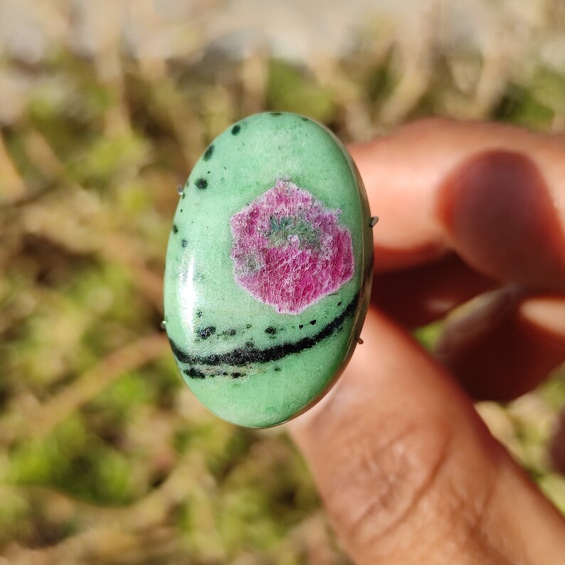 Peut inclure: Une pierre pr&eacute;cieuse ovale verte en cabochon avec des inclusions noires et une inclusion de rubis rose au centre.