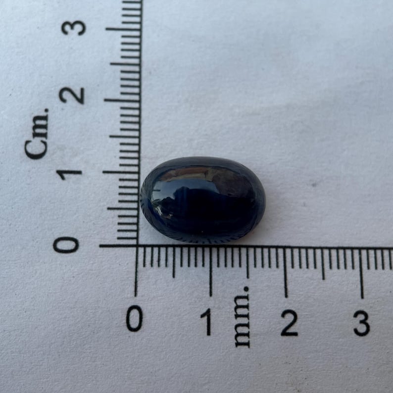 May include: A dark blue oval-shaped gemstone measuring approximately 1 cm in length.