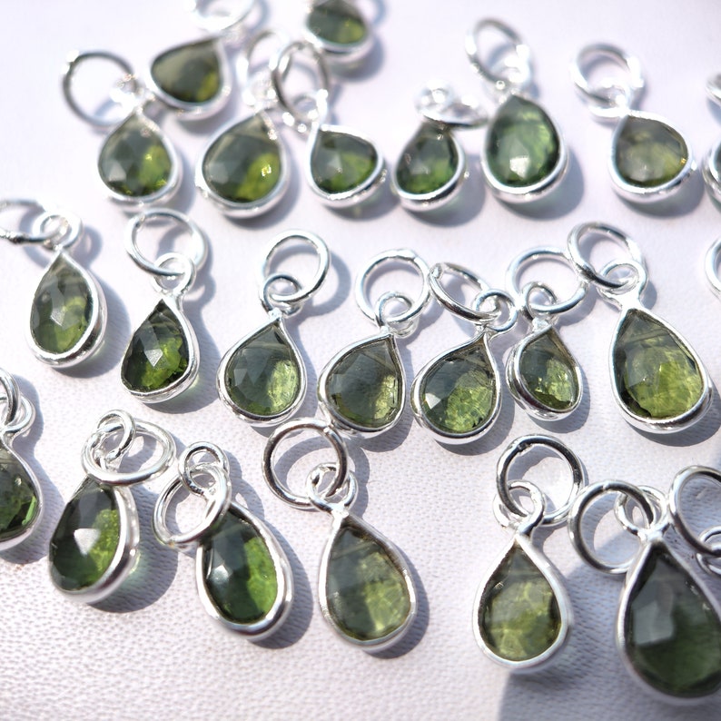 Op de afbeelding: Een verzameling groene edelsteen-traanbedels met zilveren springringen. De bedels zijn perfect om een ​​toets van glans toe te voegen aan sieradenprojecten.