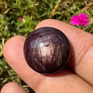 以下が含まれることがあります： 中心に星形のパターンを持つ濃い赤色の宝石。宝石は丸く、滑らかで磨かれた表面をしています。