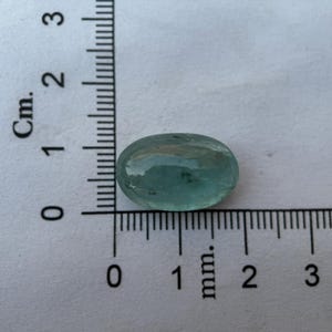 May include: A light blue oval-shaped gemstone with a smooth, polished surface. The gemstone is approximately 1 cm in length.