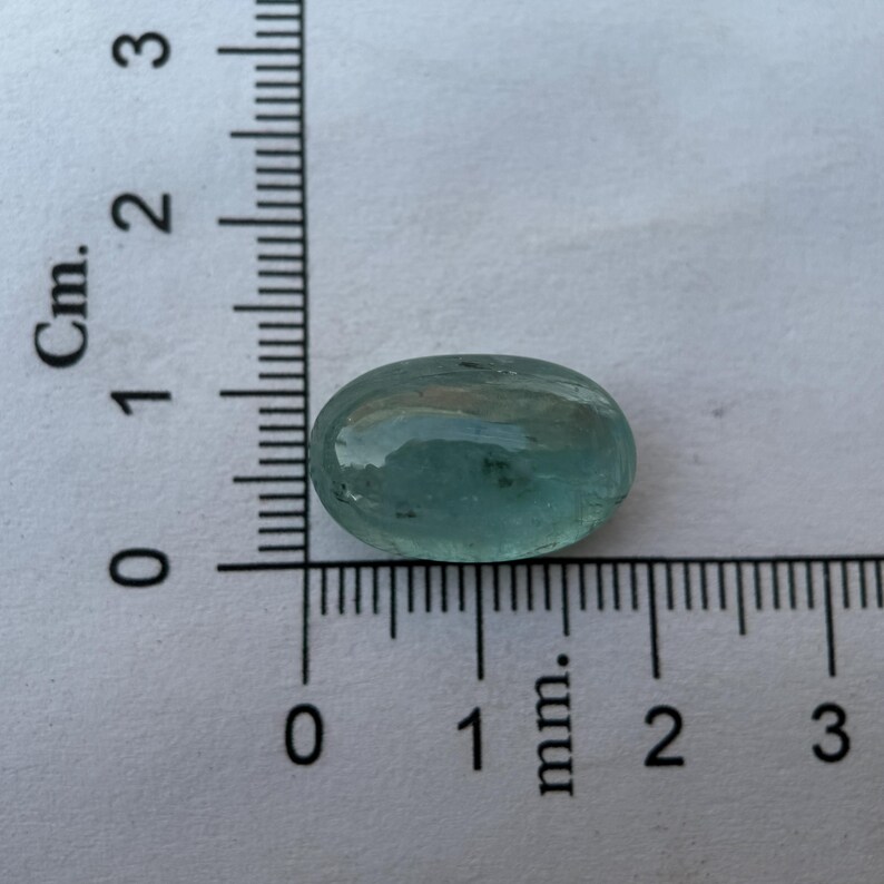 May include: A light blue oval-shaped gemstone with a smooth, polished surface. The gemstone is approximately 1 cm in length.