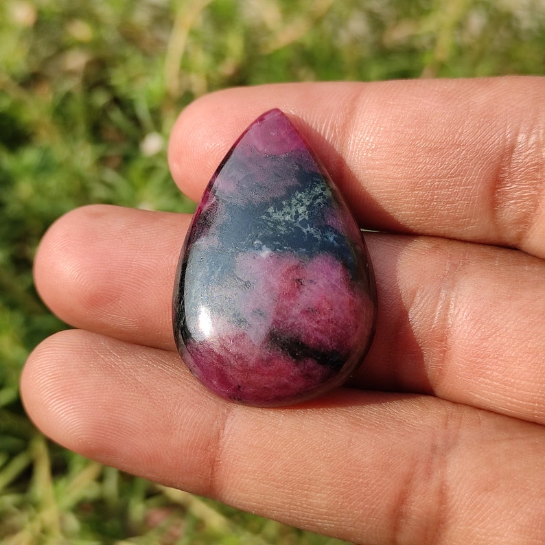 Puede incluir: Una piedra preciosa en cabuj&oacute;n en forma de l&aacute;grima con un patr&oacute;n rosa y negro. La piedra preciosa tiene un acabado brillante.
