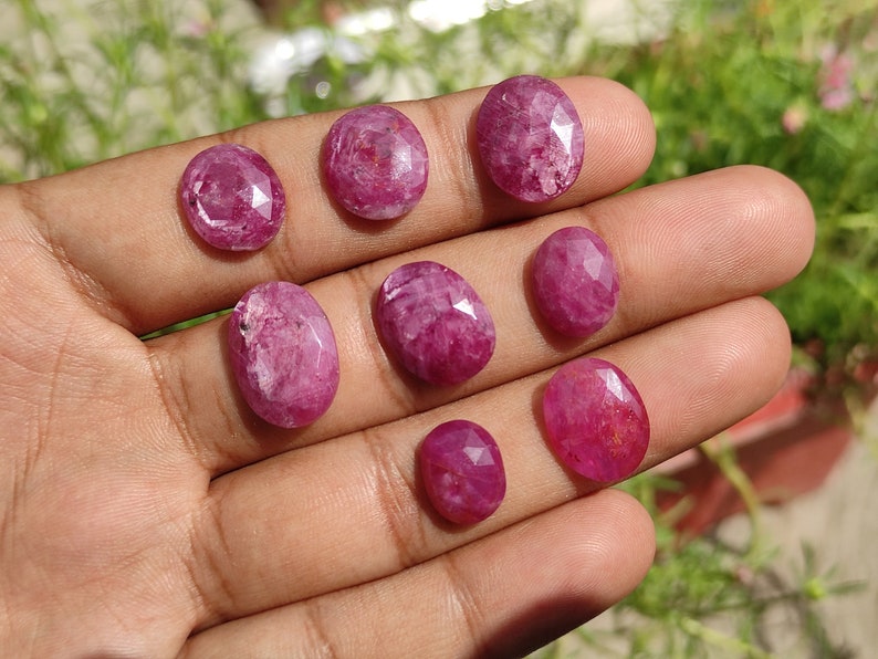 Pu&ograve; includere: Una collezione di otto pietre preziose ovali di colore rosa con taglio sfaccettato. Le pietre preziose sono esposte su una mano.