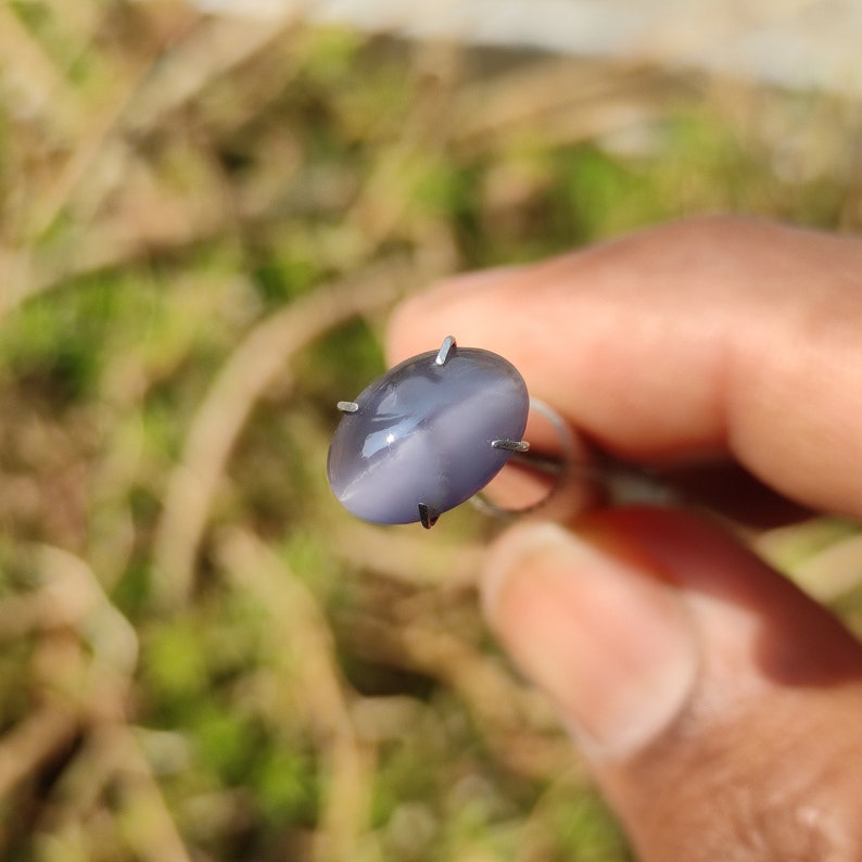 K&ouml;nnte beinhalten: Ein grauer ovaler Cabochon-Edelstein mit einem sternf&ouml;rmigen Muster in der Mitte, gehalten von einer Krappenfassung.