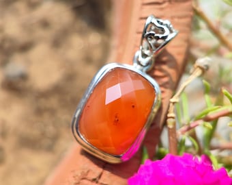May include: A silver pendant with a faceted carnelian gemstone. The pendant has a delicate, ornate design and is perfect for adding a touch of elegance to any outfit.