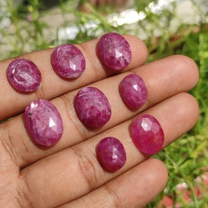 Pu&ograve; includere: Una collezione di otto pietre preziose di rubino rosa di forma ovale e sfaccettate. Le pietre preziose sono disposte in fila su una mano.