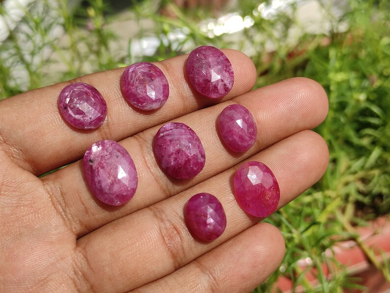 Pu&ograve; includere: Una collezione di otto pietre preziose di rubino rosa di forma ovale e sfaccettate. Le pietre preziose sono disposte in fila su una mano.