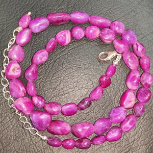 May include: A pink gemstone necklace with a silver clasp. The necklace is made of smooth, oval-shaped beads.