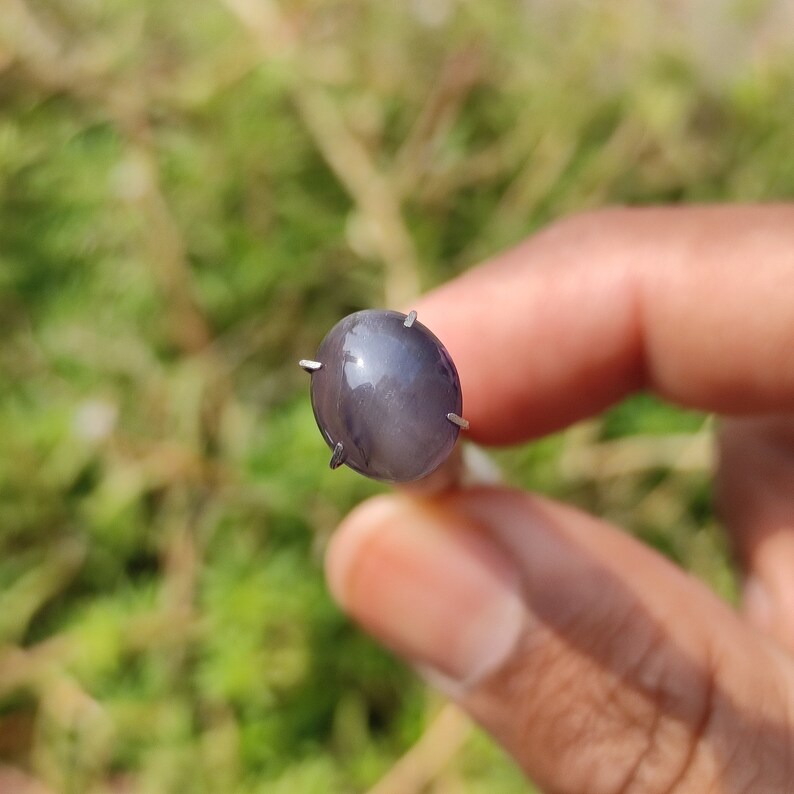 May include: A gray oval-shaped gemstone with a star-like pattern, set in a silver prong setting.