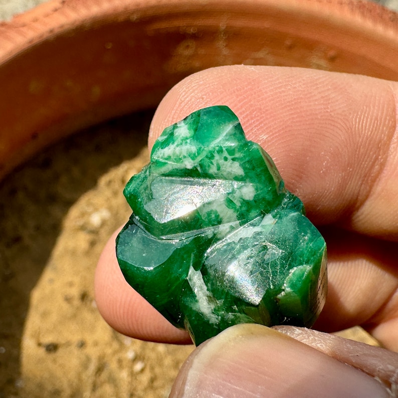 May include: A green jade stone with white veins, carved into a unique shape. The stone is being held by a hand.