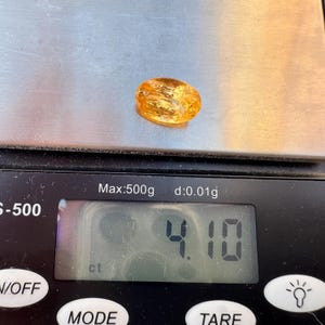 May include: A close-up of a yellow-orange gemstone on a digital scale. The scale reads 4.10 ct.