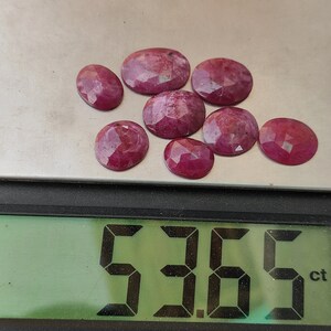 Pu&ograve; includere: Primo piano di una bilancia digitale che mostra 5,36 carati. La bilancia mostra una collezione di 9 pietre preziose di rubino sfaccettate, di diverse dimensioni e forme. I rubini sono di colore rosa intenso.