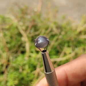 May include: A close-up of a gray gemstone with a shimmery, iridescent finish, held in a metal setting.