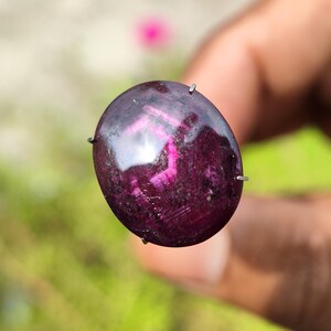 May include: A deep purple gemstone with a cabochon cut and a reflective surface. The gemstone is held in place by four prongs.