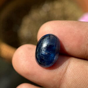 May include: A deep blue oval-shaped gemstone with a smooth, polished surface. The stone has a slight shimmer and is set in a clear, transparent setting.