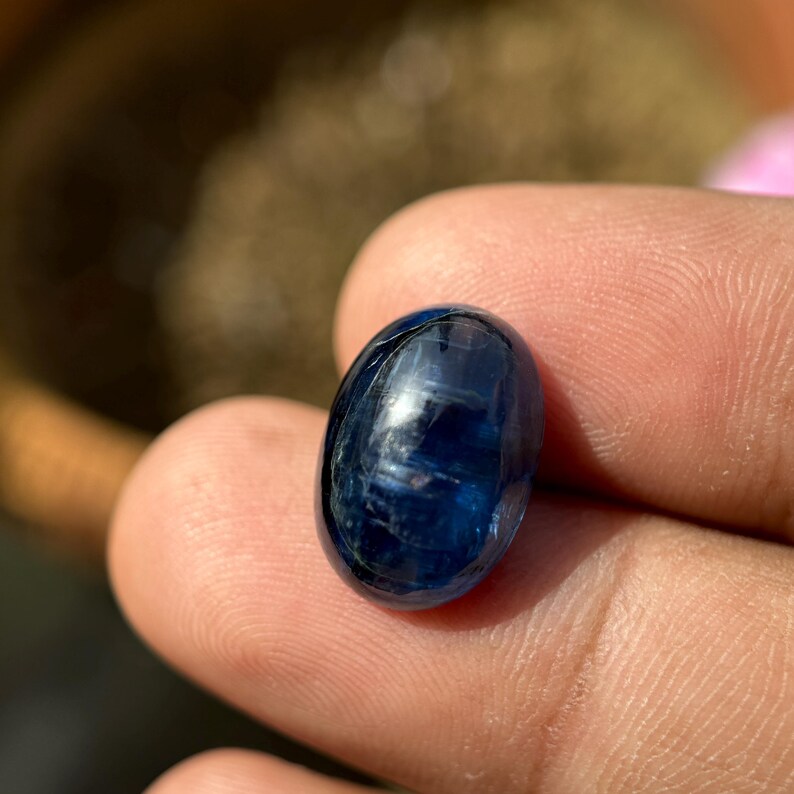 May include: A deep blue oval-shaped gemstone with a smooth, polished surface. The stone has a slight shimmer and is set in a clear, transparent setting.
