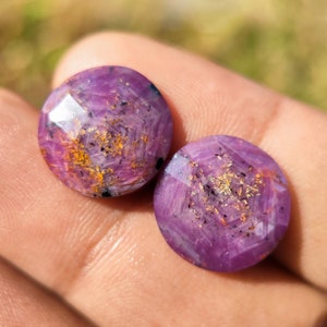 May include: Two purple and gold gemstone cabochons with a starburst pattern. The cabochons are round and have a smooth, polished surface.