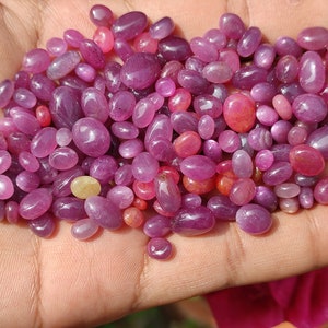May include: A handful of polished, oval-shaped gemstones in shades of pink and red. The gemstones vary in size and have a smooth, glossy surface. A few stones have a yellowish hue.