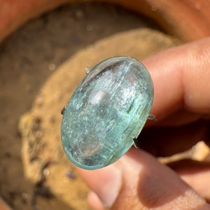 Puede incluir: Una piedra preciosa ovalada de color azul claro en cabujón con una superficie lisa y pulida. La piedra preciosa está engastada en un engaste de garras de plata.