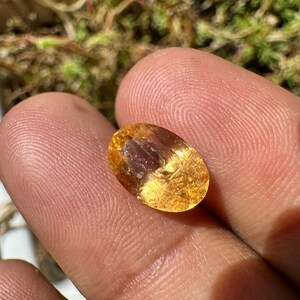 May include: A golden yellow oval-shaped gemstone with a slight reddish hue and visible internal inclusions.