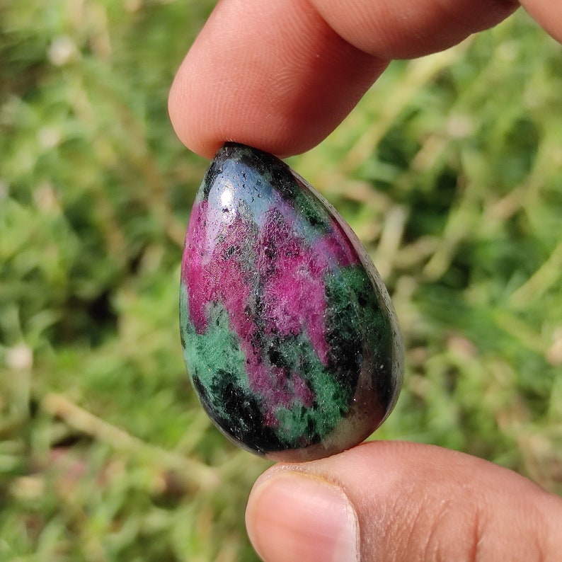 May include: A teardrop-shaped green and pink gemstone pendant with a smooth, polished surface.