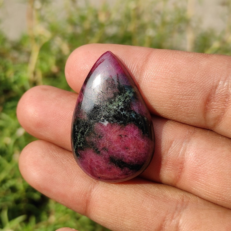 Puede incluir: Un colgante de piedra tallada en cabuj&oacute;n en forma de l&aacute;grima con un patr&oacute;n de color rosa y verde. La piedra est&aacute; pulida y tiene un acabado liso y brillante.