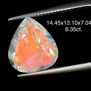 May include: A clear, faceted gemstone with a pink hue and iridescent rainbow colors. The gemstone is shaped like a teardrop and measures 14.45x13.10x7.04mm, weighing 6.35 carats.