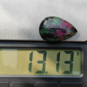 May include: A green, pink, and black gemstone cabochon weighing 13.13 grams on a digital scale.