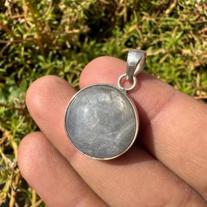 May include: A silver pendant featuring a round, grey, iridescent gemstone with a silver bail.