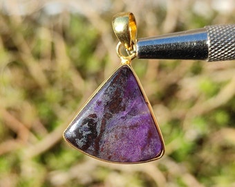 Pode incluir: Um pingente de ouro com uma gema roxa e preta de forma triangular.