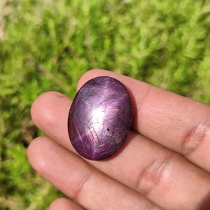 May include: A deep purple star ruby gemstone with a cabochon cut and a star-like pattern in the center.