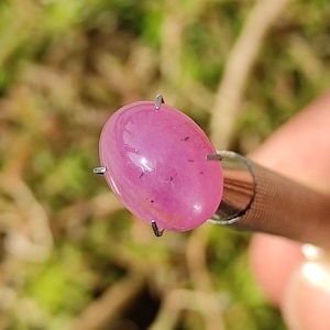 Puede incluir: Una piedra preciosa ovalada de color rosa con un alto pulido, engastada en un engaste de garras de metal.