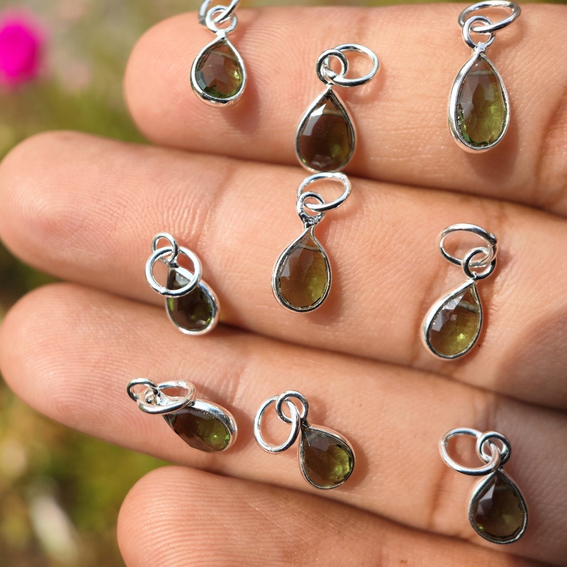 Op de afbeelding: Tien zilveren traanvormige hangers met groene edelstenen. Elke hanger heeft een kleine lus aan de bovenkant om aan een ketting of andere sieraden te bevestigen.