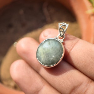 May include: A silver pendant with a round, light green gemstone. The pendant has a delicate, ornate design.