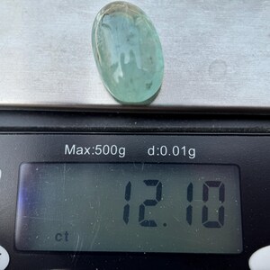 May include: A light blue oval gemstone weighing 12.10 carats on a digital scale.