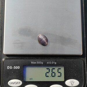 K&ouml;nnte beinhalten: Nahaufnahme eines grauen Edelsteins auf einer digitalen Waage. Die Waage zeigt 2,65 ct an.