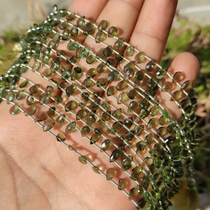 May include: A strand of green gemstone beads, each bead is faceted and pear-shaped. The beads are strung on a silver wire.
