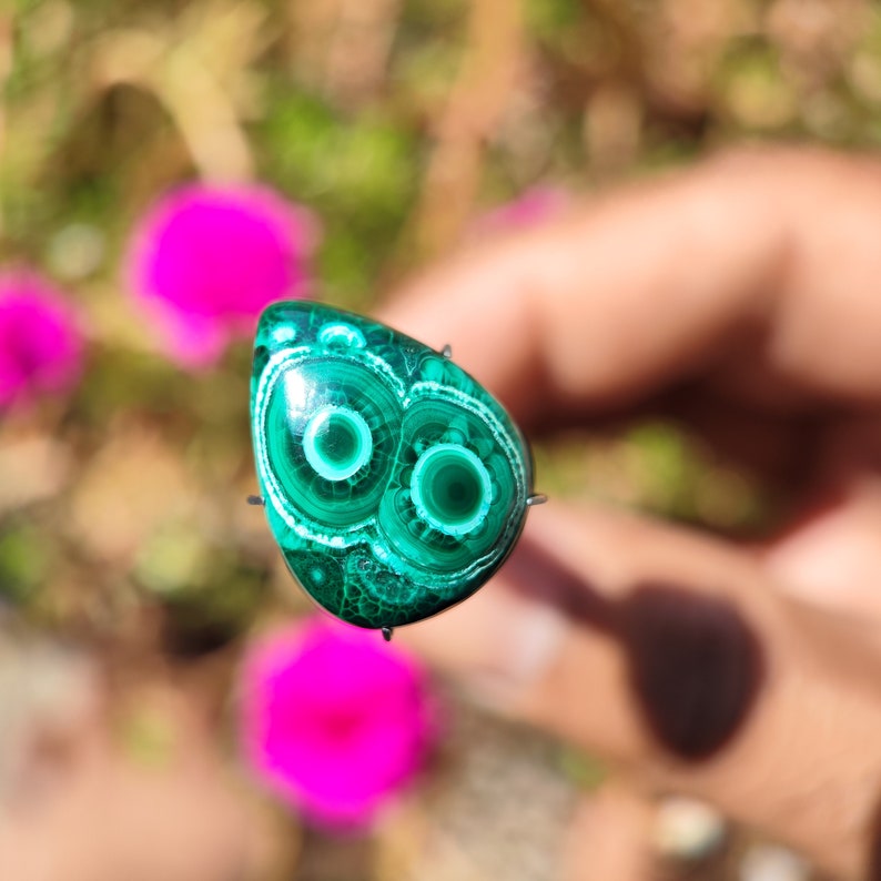 May include: A green malachite cabochon with white concentric circles, set in a teardrop shape.