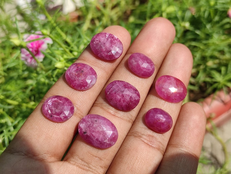 Pu&ograve; includere: Otto pietre preziose rosa di forma ovale con bordi sfaccettati. Le pietre preziose sono esposte su una mano.