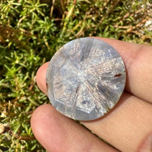 May include: A round, silver-colored gemstone with a starburst pattern. The gemstone is about 2 inches in diameter and has a smooth, polished surface.
